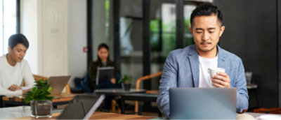 Three people are working on laptops while seated at tables in a modern office setting.