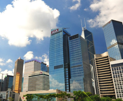 Et bylandskap av høye, moderne skyskrapere på en solfylt dag med blå himmel og spredte skyer.