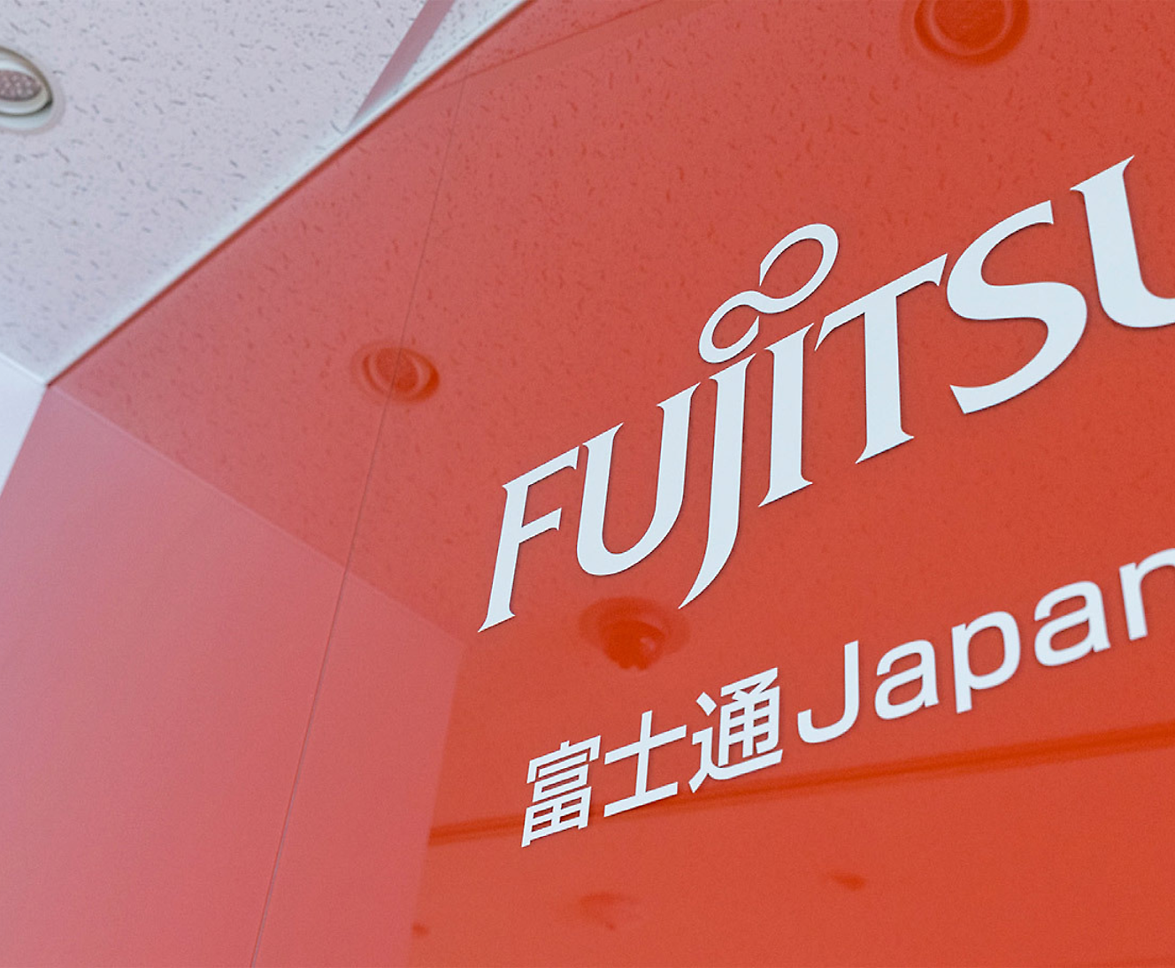 Primo piano parziale di un'insegna fujitsu con logo e testo giapponese su uno sfondo rosso, prospettiva angolata 