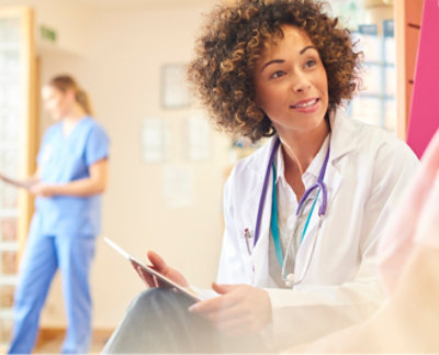 곱슬머리를 가진 의사가 환자와 대화하며 클립보드를 들고 있습니다.