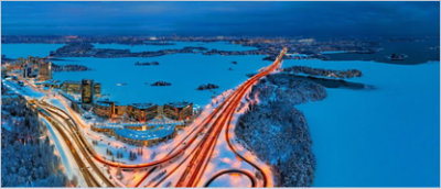 An aerial view of a cityscape featuring illuminated highways winding through snow-covered terrain