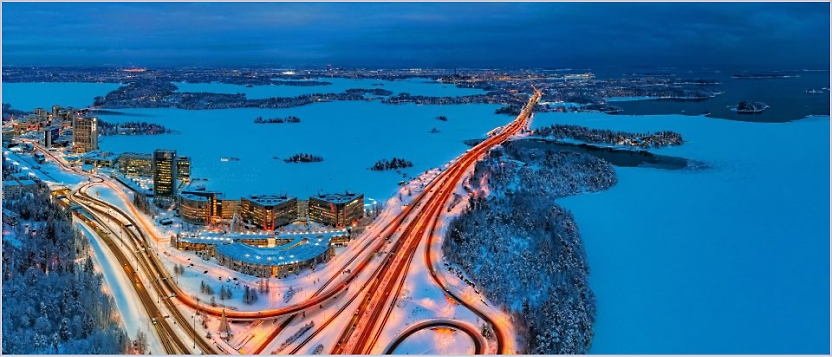 An aerial view of a cityscape featuring illuminated highways winding through snow-covered terrain