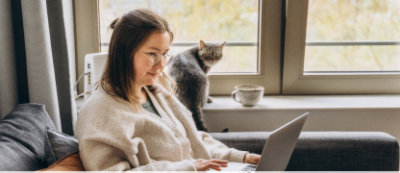 A girl sitting in front of a computer with a cat in the background