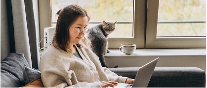 A girl sitting in front of a computer with a cat in the background