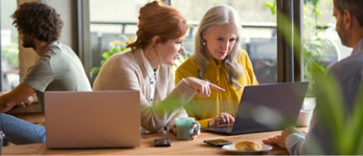 To kvinner sitter ved et bord og arbeider på en bærbar datamaskin, en peker på skjermen mens den andre observerer.Bakgrunn.