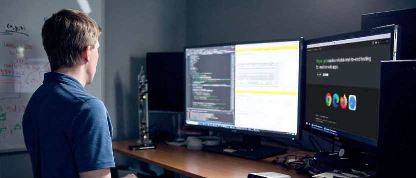 Een man in een kantoor die kijkt naar meerdere computerschermen met code- en gegevensvisualisaties.