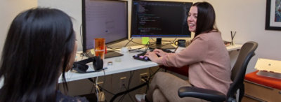 A person sitting their desk playing a first person shooter video game on a computer monitor.