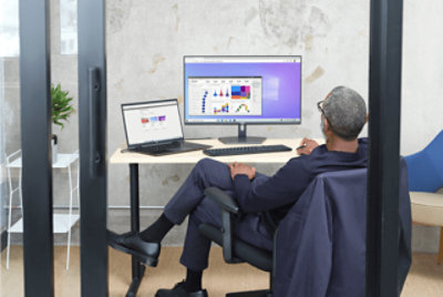 A person working at a desk with a laptop connected to a desktop monitor in their office 
