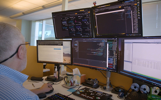 Человек, работающий за своим столом с пятью экранами, отображающими данные и приложения