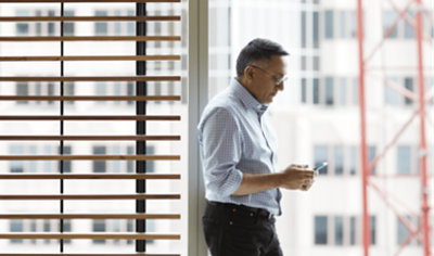 A person looking into his mobile while standing near a window