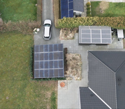 Luftbild eines Hauses mit Solarmodulen auf dem Dach, ein Auto ist in der Einfahrt geparkt