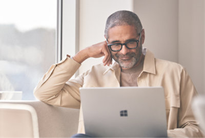 A man with glasses smiling, sitting in front of a laptop.