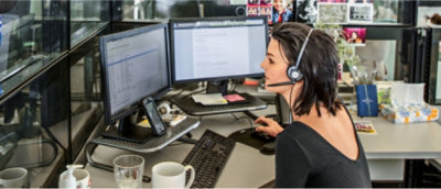 A person with a headset works at a desk with two computer monitors displaying documents.