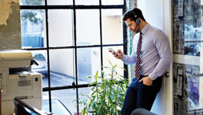 A man wears Jabra Evolve 65 while checking his phone at work.