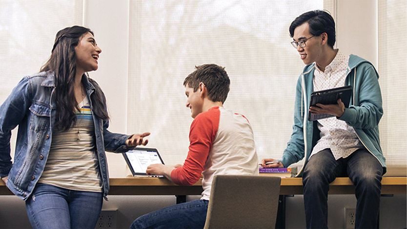 Tre studenter samarbeider med en Surface-enhet.