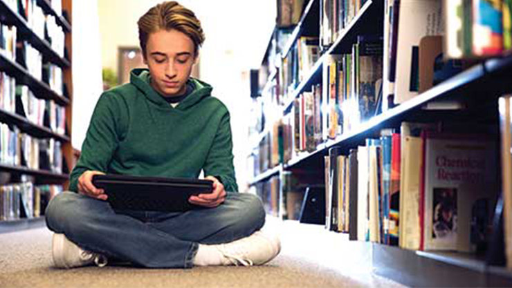 Schüler sitzt mit Laptop auf dem Boden in der Bibliothek