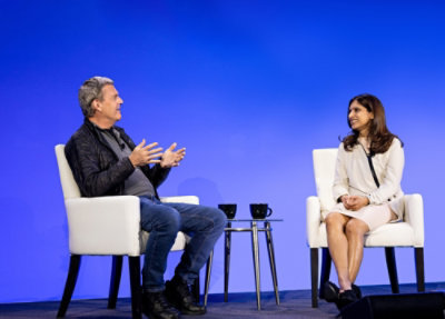 aria-label A man and woman talking to each other while sitting in white chairs.