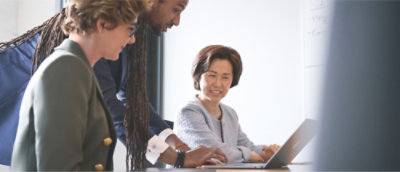 Trois personnes discutent dans un bureau. Une personne utilise un ordinateur portable pendant que les autres regardent.