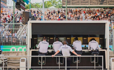 Mercedes Formula 1 pit wall team monitoring race data with track and crowd in background