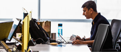Person working at a cluttered office desk with multiple monitors.