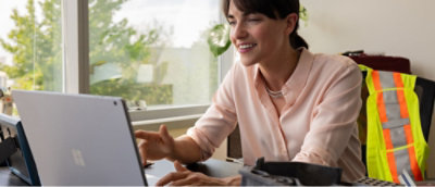 A woman sitting at a desk by a large window, working on a laptop