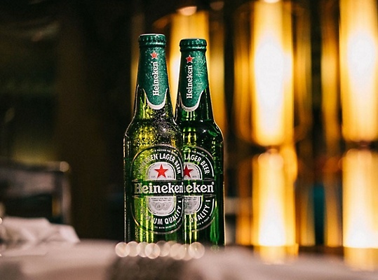 Two Heineken beers on a bar.