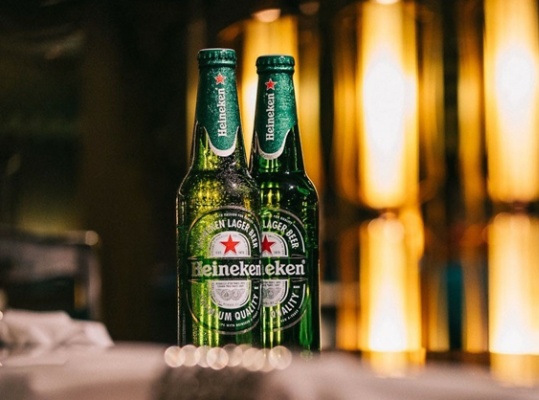 Two Heineken beers on a bar.