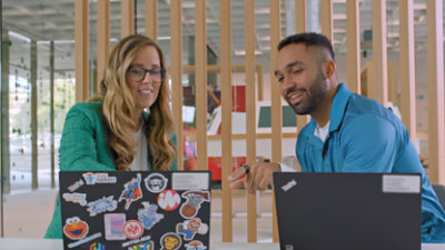 Two people collaborating at a table with laptops in a modern office setting. 