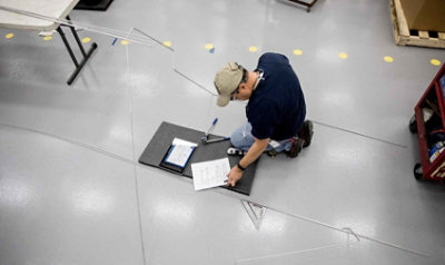 A person kneeling down and looking at a tablet and paperwork on the floor