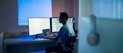 A man sitting at a desk with a laptop and several computer screens.
