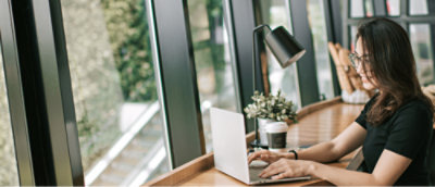 Person working on a laptop at a desk by a window with a view of trees.