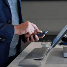 A person using a mobile phone while standing in front of a desktop monitor 