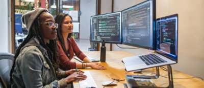 a woman sitting at a desk with two computer screens