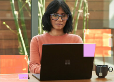 一位戴眼鏡、穿著紅色襯衫的女士，坐在桌前使用膝上型電腦。