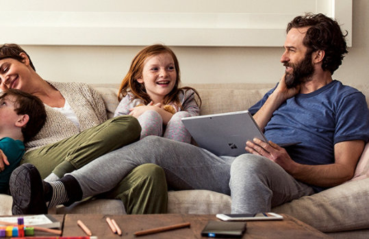 Family sitting together on the couch using a laptop and tablet.