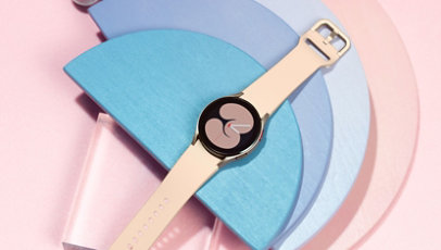A Samsung Galaxy Watch 4 in Pink Gold sitting on a pink and blue decorative background. 