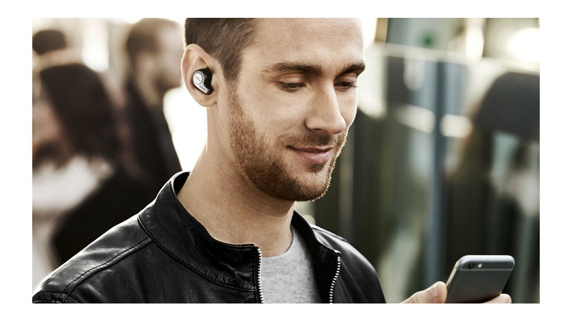 A man checks his phone while wearing Jabra Elite earbuds in a crowded space.