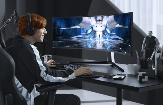A person sitting at a desk in front of the Samsung Odyssey Neo Mini Gaming Monitor.