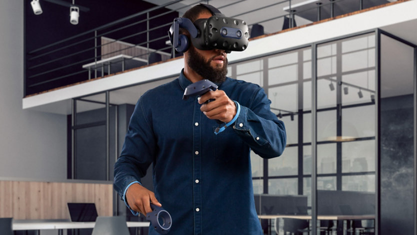 Man wearing Vive V R headset while holding two wireless controllers. 