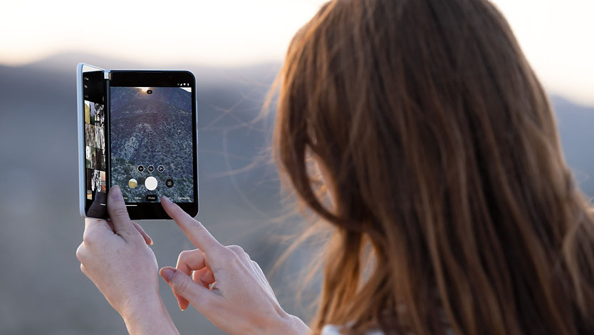Une personne tenant un Surface Duo 2 et utilisant ses doigts pour interagir à l’écran.