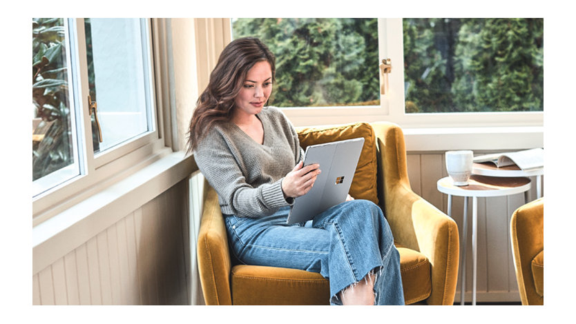 A woman uses a Surface tablet while relaxing at home.
