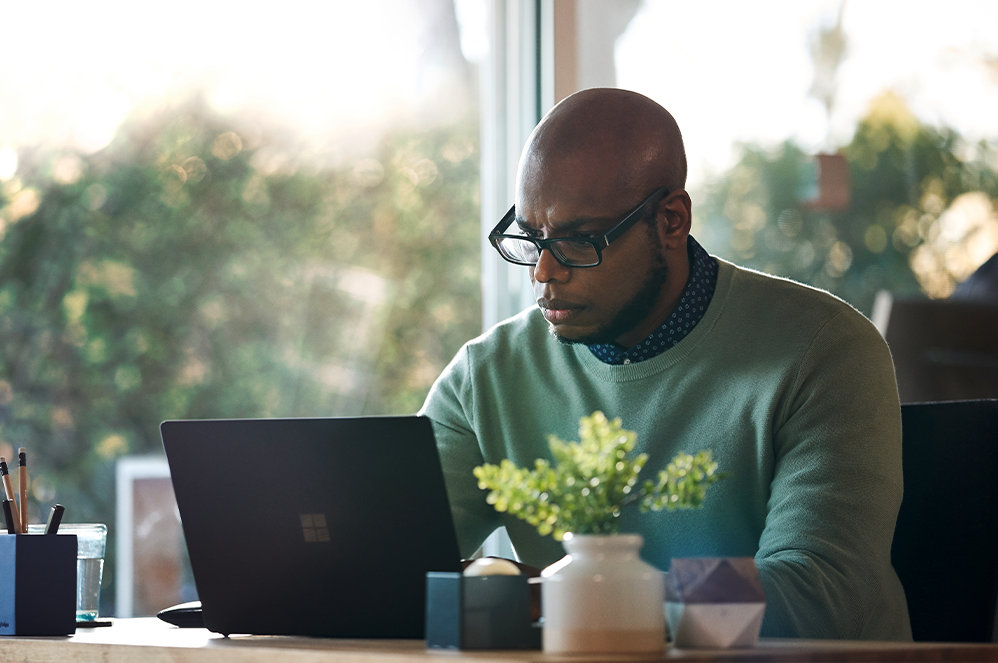 En person, der bruger Project, sidder ved et skrivebord bag en åben Surface Laptop.