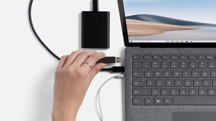 Adult hands working on Surface Laptop 4 in Platinum plugging multiple devices into USB ports