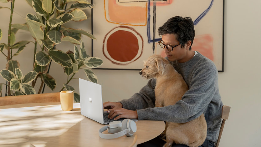 An adult male using Surface laptop 4 13 inch Platinum with dog on his lap