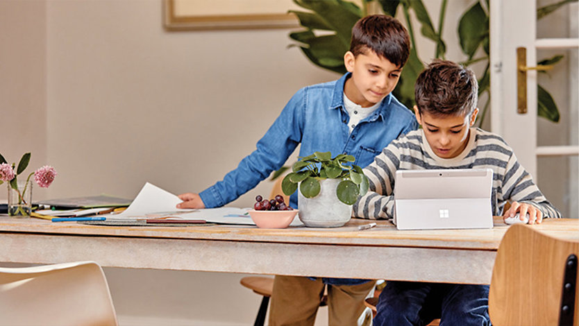 Two young students working at a desk with a surface laptop.