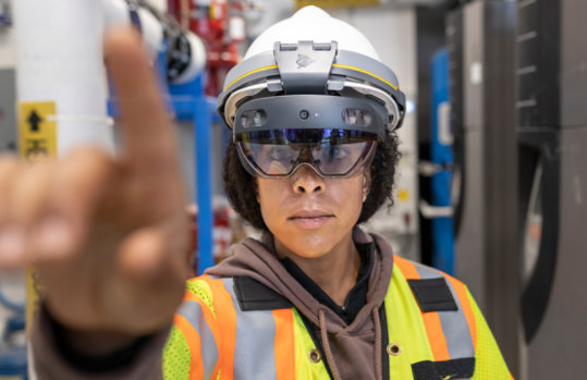 A person experiences mixed reality using the Trimble XR 10 with HoloLens 2 in an industrial environment reaching towards the viewer. 