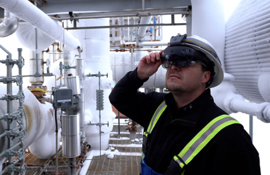 A person in an industrial setting wears the Trimble XR 10 with HoloLens 2 while inspecting pipes. 