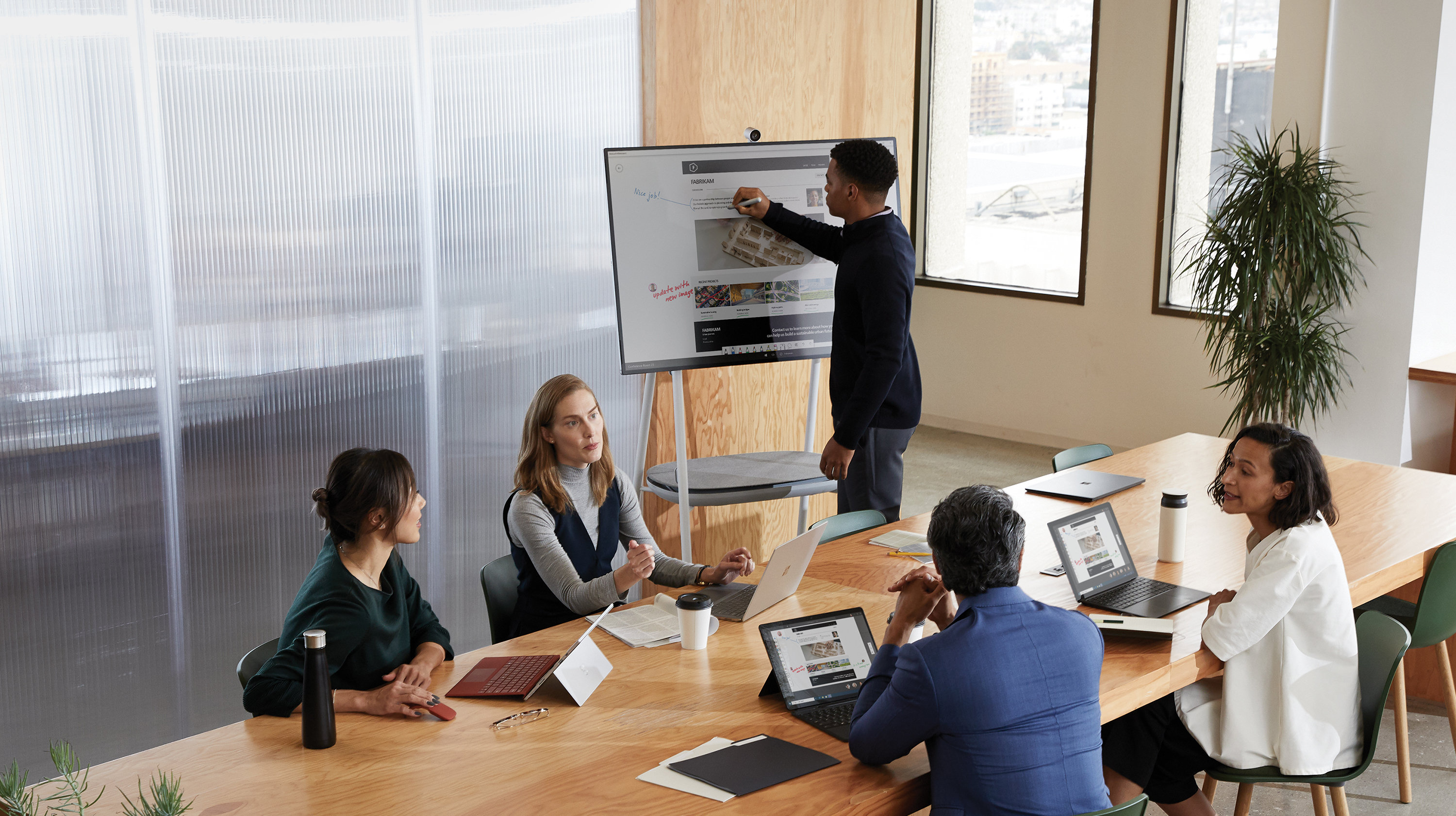 Fünf Erwachsene arbeiten mit einem Mann zusammen und benutzen dazu ein Microsoft Surface Hub.