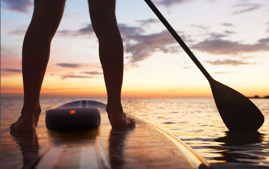 A person paddleboarding in the ocean with the JBL Flip5 speaker.