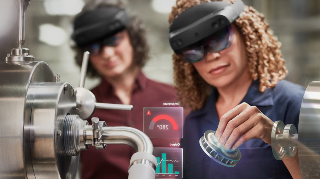 Eine Frau benutzt ein HoloLens-Gerät bei der Arbeit, während eine andere Mitarbeiterin sie dabei beobachtet.